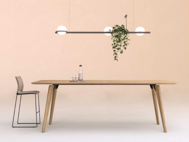 A rectangular oak veneer meeting table with an overhead long floating light which has a plant on it hanging down. The table has a singular high framed brown chair sitting at the head of the table.